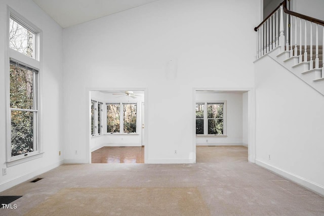 unfurnished living room with carpet flooring, visible vents, a healthy amount of sunlight, and a towering ceiling