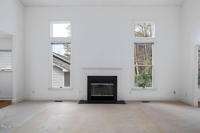 unfurnished living room featuring a high ceiling, a fireplace with flush hearth, visible vents, and carpet floors