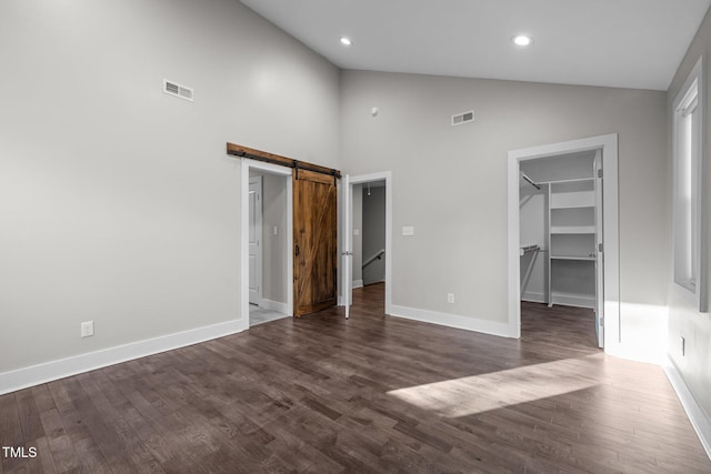 unfurnished bedroom with a closet, a barn door, dark hardwood / wood-style floors, and a spacious closet