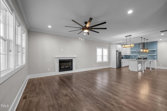 unfurnished living room featuring dark hardwood / wood-style flooring, sink, crown molding, and ceiling fan