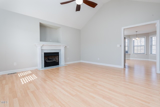 unfurnished living room with high vaulted ceiling, light wood-type flooring, ceiling fan with notable chandelier, and a fireplace