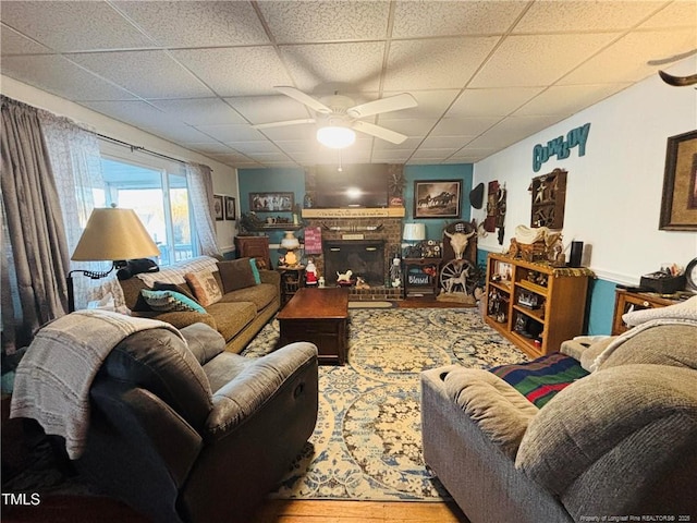 living room featuring ceiling fan, a fireplace, and a drop ceiling