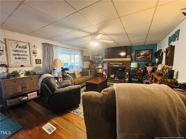 living room featuring wood-type flooring, a brick fireplace, a paneled ceiling, and ceiling fan