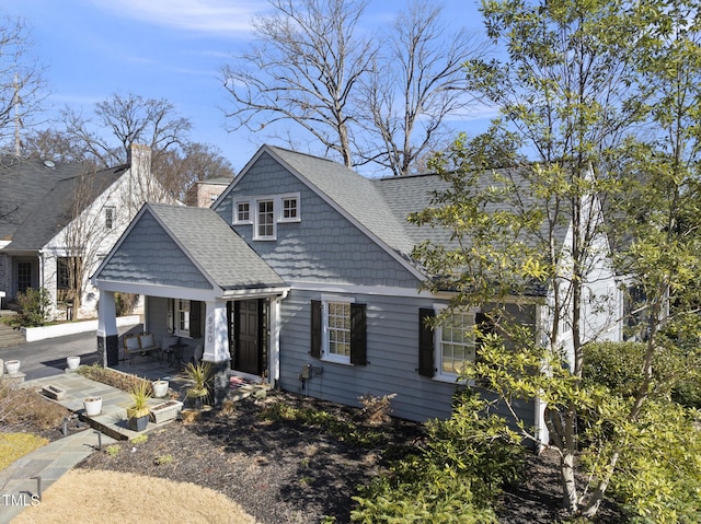 view of front facade featuring a shingled roof, a chimney, and a porch