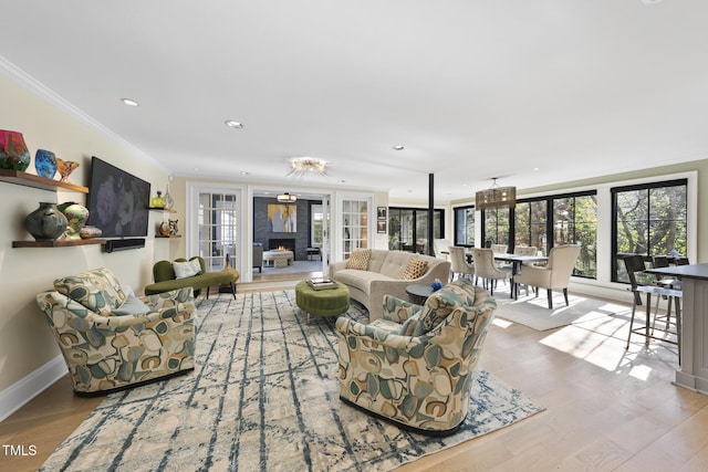 living area featuring a warm lit fireplace, crown molding, baseboards, and wood finished floors