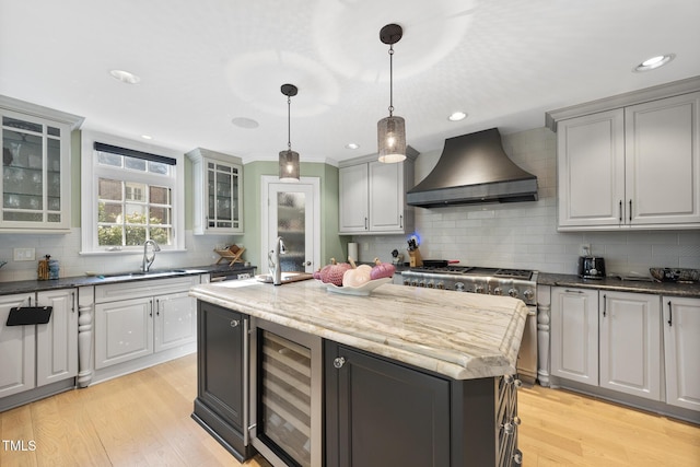 kitchen with beverage cooler, light wood-style flooring, high end stainless steel range oven, custom exhaust hood, and a sink