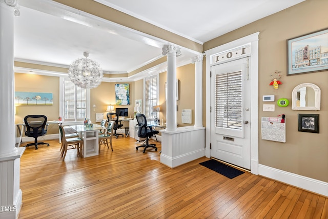 foyer entrance featuring an inviting chandelier, crown molding, decorative columns, and light hardwood / wood-style floors