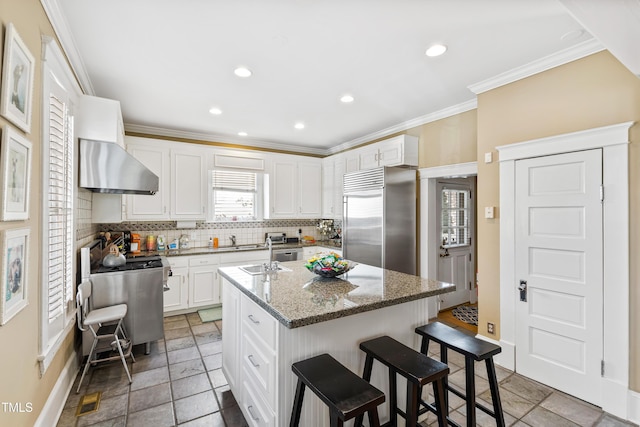 kitchen with a breakfast bar area, stone counters, a kitchen island with sink, range, and built in fridge