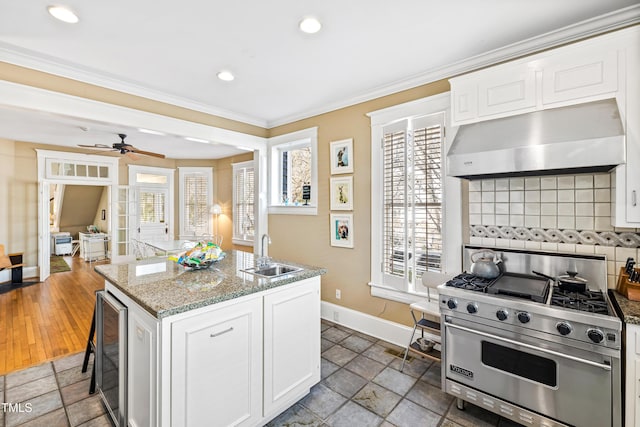 kitchen with white cabinetry, an island with sink, sink, wine cooler, and designer range