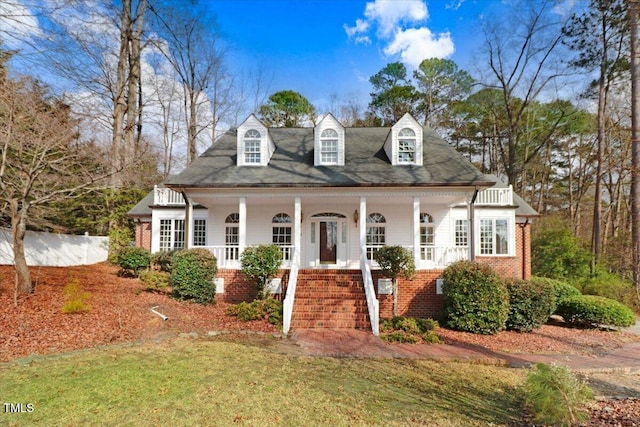 cape cod-style house featuring covered porch and a front lawn