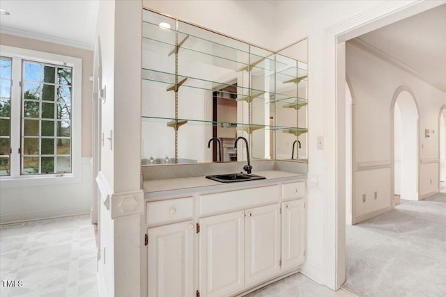 bar featuring sink, light carpet, ornamental molding, a wealth of natural light, and white cabinets