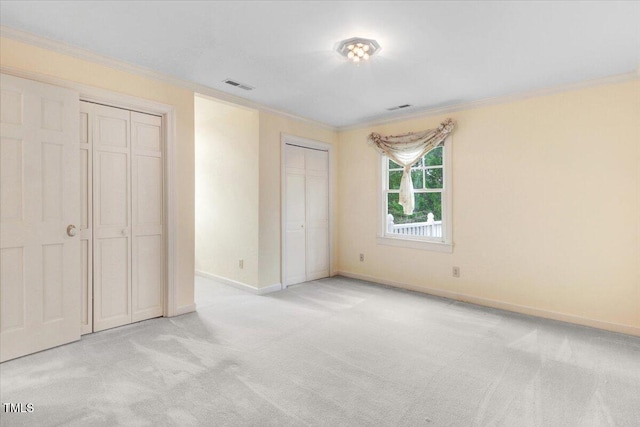 unfurnished bedroom with crown molding, light carpet, and two closets