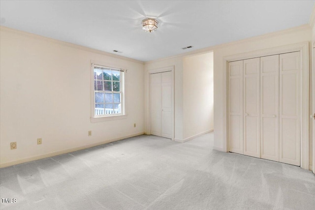 unfurnished bedroom with crown molding, light carpet, and two closets