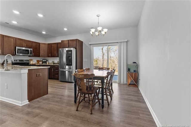 kitchen featuring an inviting chandelier, wood-type flooring, decorative light fixtures, stainless steel appliances, and light stone countertops