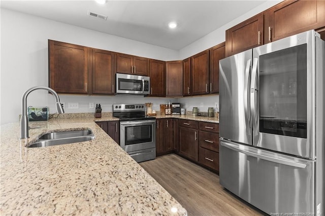 kitchen with hardwood / wood-style flooring, appliances with stainless steel finishes, sink, and light stone counters