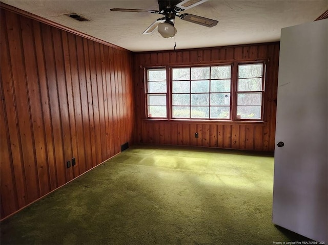 empty room with ceiling fan, carpet, and wooden walls