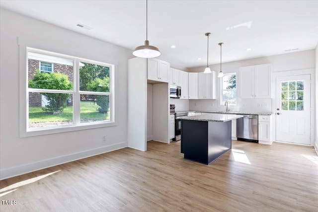 kitchen with light stone counters, white cabinetry, stainless steel appliances, and a center island