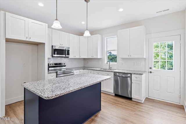 kitchen with appliances with stainless steel finishes, decorative light fixtures, white cabinets, a center island, and light stone counters