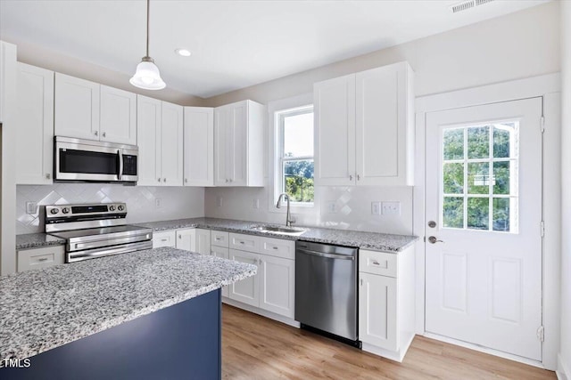 kitchen featuring sink, appliances with stainless steel finishes, white cabinetry, hanging light fixtures, and light wood-type flooring