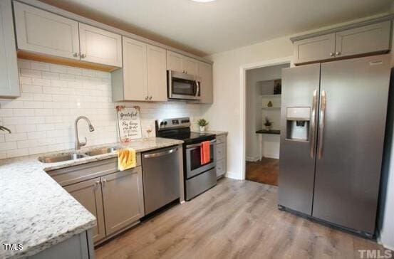 kitchen featuring sink, gray cabinetry, backsplash, light stone counters, and stainless steel appliances