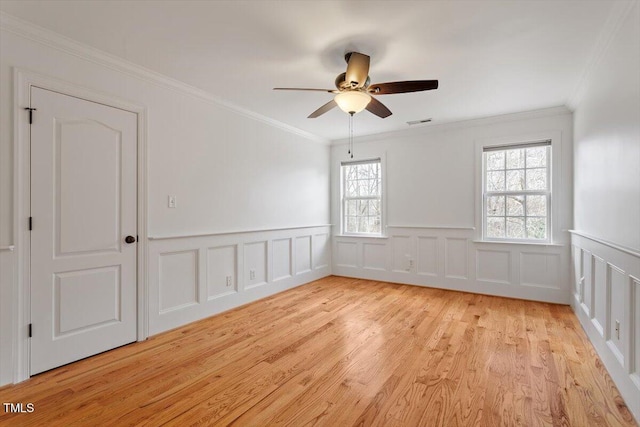 spare room featuring light wood finished floors, visible vents, a decorative wall, ornamental molding, and a ceiling fan