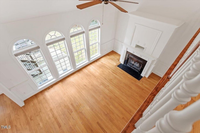 living room featuring a ceiling fan, a fireplace with flush hearth, vaulted ceiling, light wood-type flooring, and a decorative wall