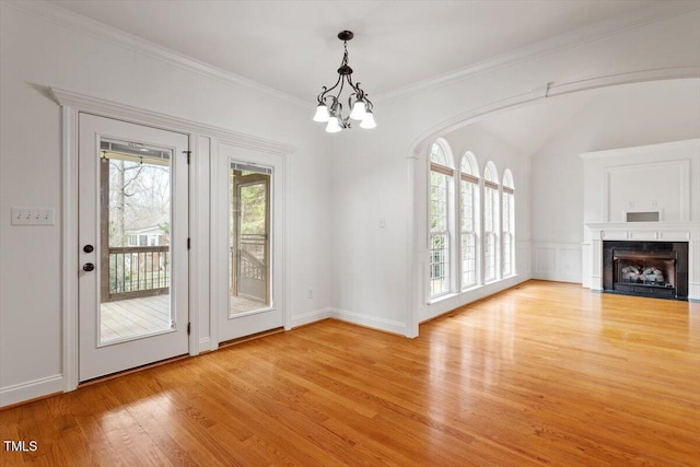 interior space with a fireplace with flush hearth, ornamental molding, light wood-type flooring, a decorative wall, and a notable chandelier