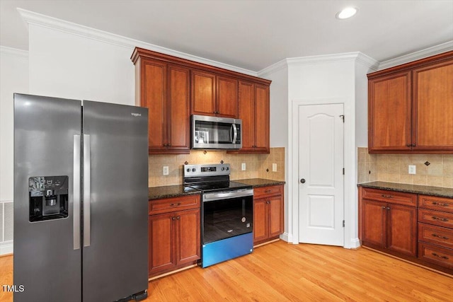 kitchen with light wood-style floors, appliances with stainless steel finishes, dark stone counters, tasteful backsplash, and crown molding