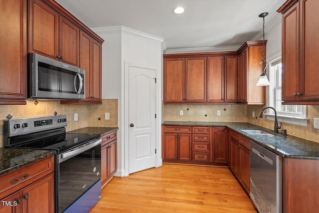 kitchen with appliances with stainless steel finishes, ornamental molding, decorative light fixtures, light wood-type flooring, and a sink