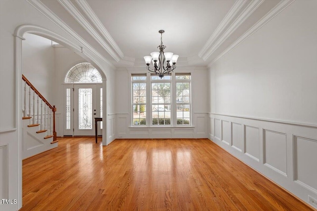 entrance foyer with light wood-style flooring, a decorative wall, stairs, an inviting chandelier, and crown molding