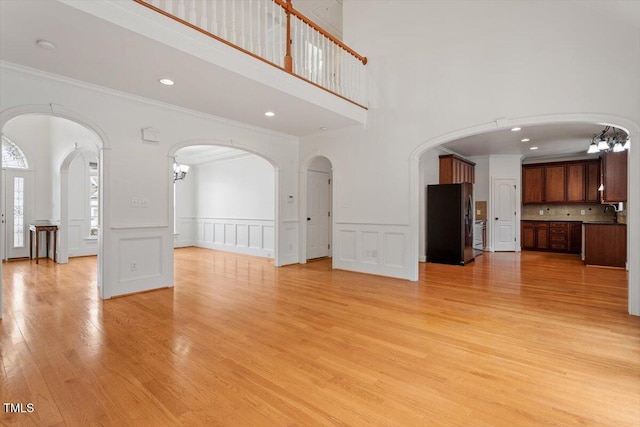 unfurnished living room featuring arched walkways, ornamental molding, light wood-style flooring, and a decorative wall