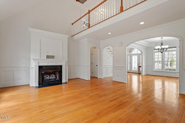 unfurnished living room featuring arched walkways, a notable chandelier, light wood finished floors, a decorative wall, and a fireplace with flush hearth