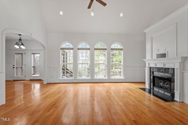 unfurnished living room featuring a decorative wall, vaulted ceiling, wood finished floors, a tile fireplace, and ceiling fan with notable chandelier