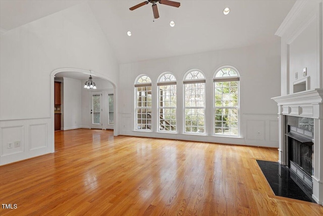 unfurnished living room featuring a tile fireplace, a decorative wall, arched walkways, and ceiling fan with notable chandelier