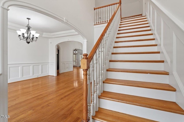 staircase with arched walkways, a notable chandelier, a decorative wall, ornamental molding, and wood finished floors