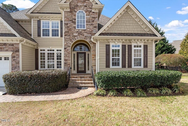 view of front facade featuring a front yard, a garage, stone siding, and a shingled roof