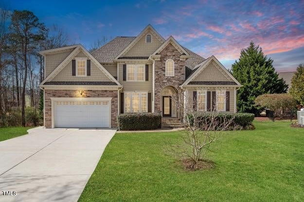 craftsman inspired home featuring stone siding, a lawn, and concrete driveway