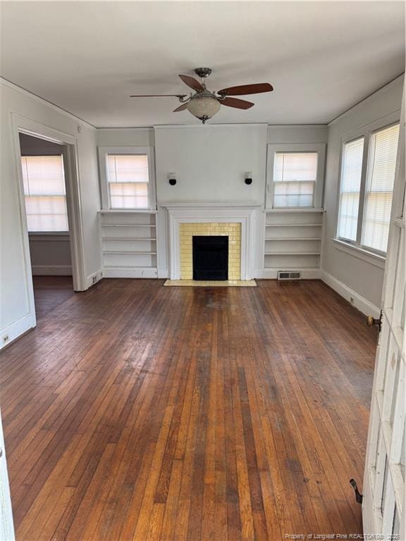 unfurnished living room with a healthy amount of sunlight, a brick fireplace, dark wood-type flooring, and ceiling fan