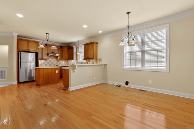 kitchen featuring a kitchen bar, tasteful backsplash, hanging light fixtures, ornamental molding, and stainless steel fridge