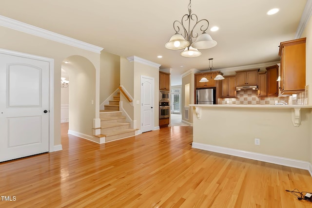 kitchen with light wood-type flooring, ornamental molding, appliances with stainless steel finishes, pendant lighting, and backsplash