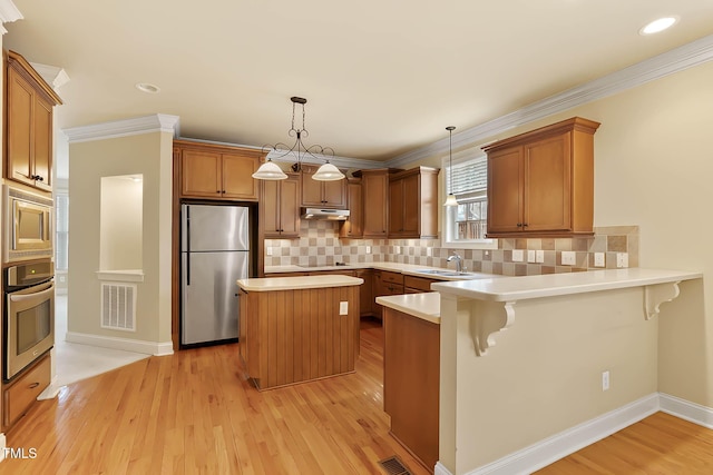 kitchen featuring a kitchen bar, light hardwood / wood-style flooring, kitchen peninsula, pendant lighting, and stainless steel appliances