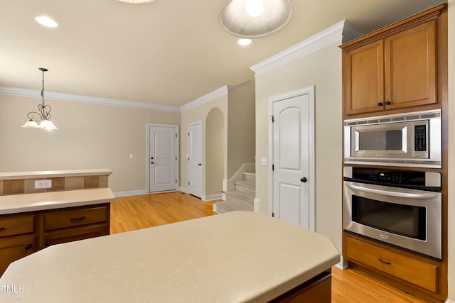 kitchen with appliances with stainless steel finishes, pendant lighting, light hardwood / wood-style floors, crown molding, and an inviting chandelier