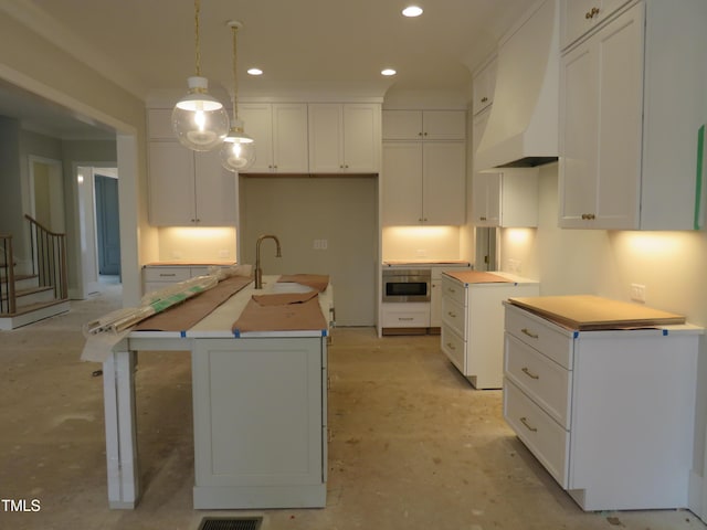 kitchen with hanging light fixtures, custom range hood, a center island with sink, and white cabinets