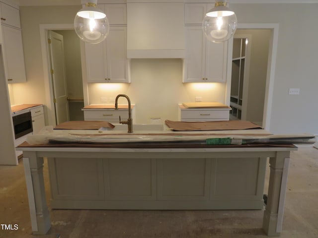 kitchen featuring a kitchen island with sink, decorative light fixtures, and white cabinets