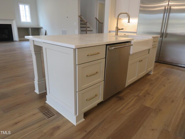 kitchen with a sink, appliances with stainless steel finishes, wood finished floors, and white cabinetry