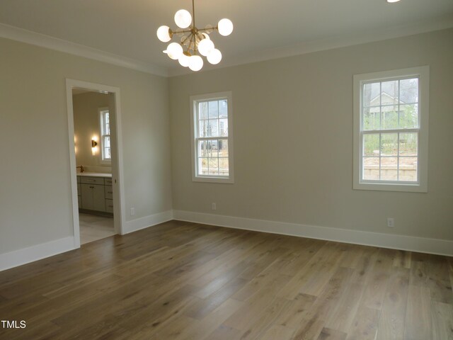 unfurnished room with baseboards, a notable chandelier, wood finished floors, and crown molding