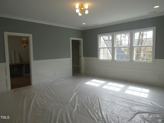 unfurnished bedroom with multiple windows, ornamental molding, and wainscoting
