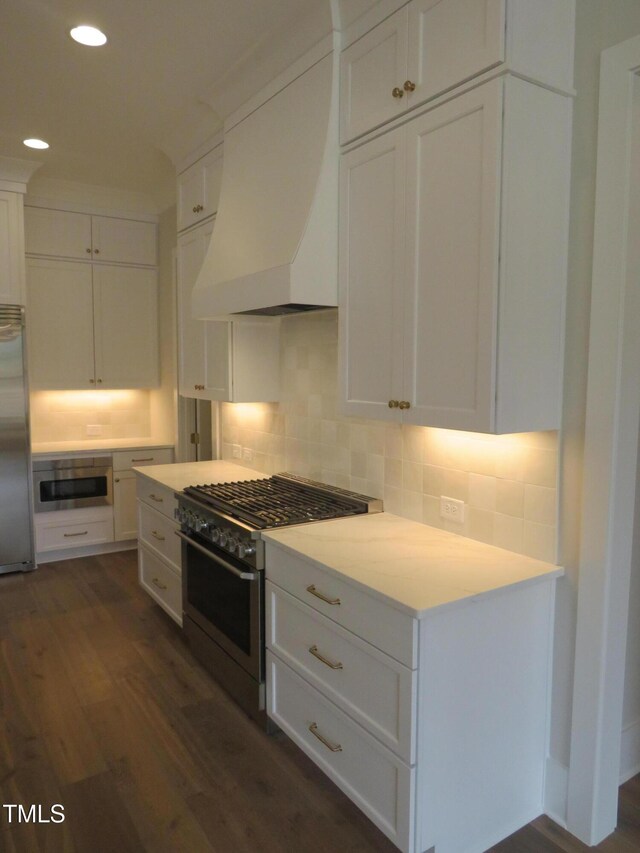 kitchen featuring dark wood-style floors, appliances with stainless steel finishes, white cabinetry, and premium range hood