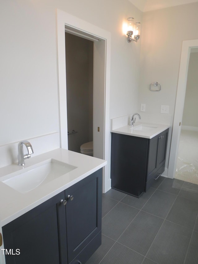 bathroom featuring tile patterned floors, toilet, two vanities, and a sink