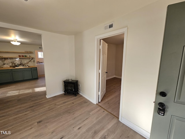 empty room with washer / dryer, sink, a wood stove, and light hardwood / wood-style floors